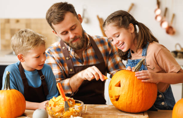 Children and dad making Jack-o-Lantern together at home, carving Halloween pumpkin Happy kids boy and girl helping father to carve Halloween pumpkin while standing in kitchen at home and preparing for autumn holiday, family children and dad making Jack-o-Lantern together happy halloween pumpkin stock pictures, royalty-free photos & images