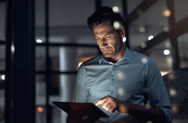 Business man, tablet and working late at night while browsing the internet, doing online research or checking trading stats. Serious entrepreneur using information technology for digital marketing