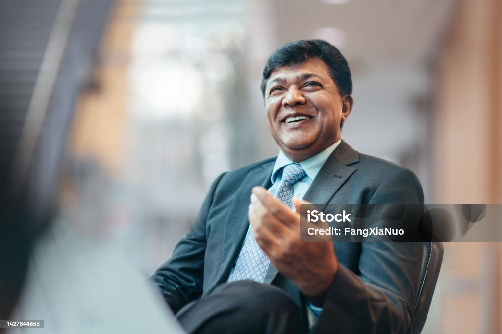 Asian Indian mature businessman talking and laughing with colleague during meeting in business office wearing suit Financial Advisor Stock Photo