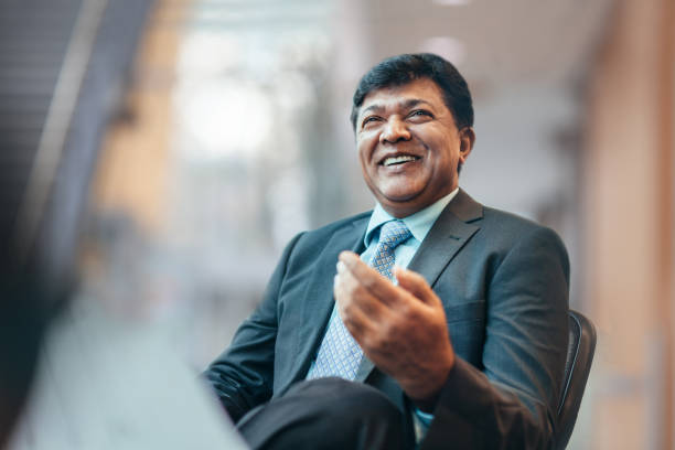 Asian Indian mature businessman talking and laughing with colleague during meeting in business office wearing suit stock photo