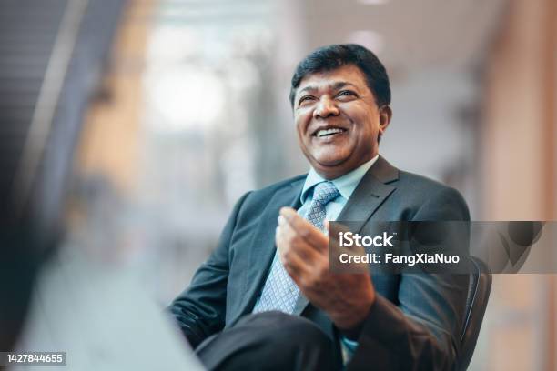 Asian Indian Mature Businessman Talking And Laughing With Colleague During Meeting In Business Office Wearing Suit Stock Photo - Download Image Now