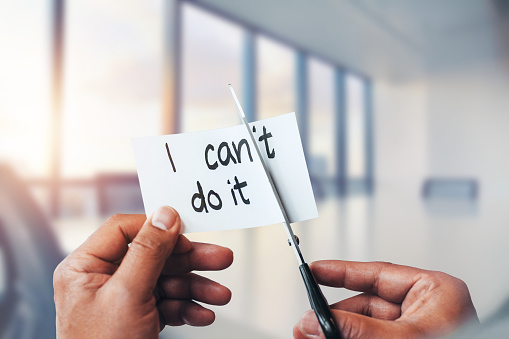 Hands of Asian African-American man cutting inspirational concept sign note in bright business office conference meeting room