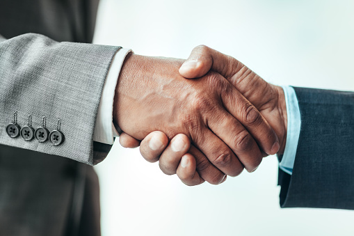 Hands of Asian African-American mature businessmen shaking hands in bright business office during meeting wearing suits