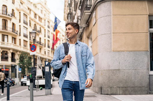 Happy young man wearing casual clothes smiling and walking in the street.