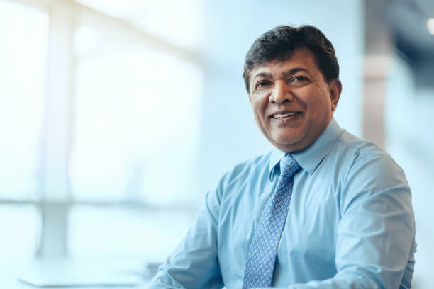 Portrait of Asian Indian mature businessman sitting smiling contented emotion bright office in businesswear stock photo