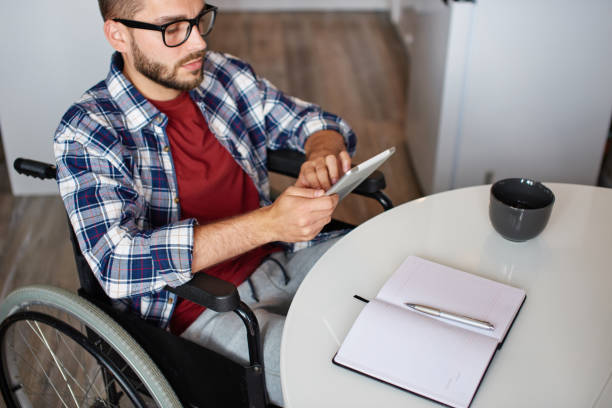 Man in wheelchair using tablet and notepad stock photo