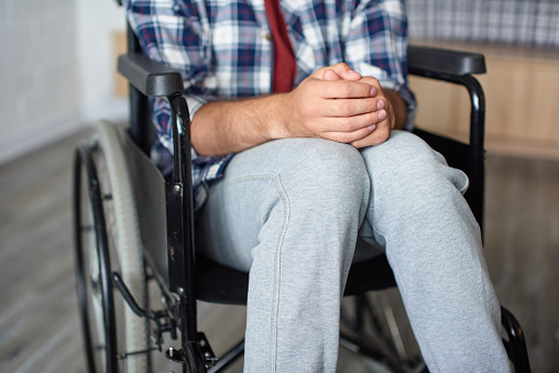 Close up of man's hands, put together on laps. He is sitting in wheelchair, can't walk