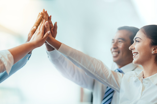 Multiracial group of business persons students stacked hands high-five in agreement achievement success aspiration smiling in bright business office classroom