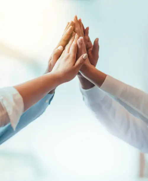 Photo of Multiracial group of students stacked hands high-five in agreement achievement success aspiration smiling in bright business office classroom