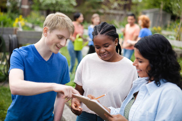 Diverse multiracial group of young volunteers coordinate plans together with mature project manager at community garden park in neighborhood environment stock photo