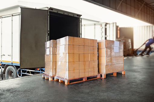 Packaging Boxes Wrapped Plastic Stacked on Pallets Loading into Cargo Container. Shipping Trucks. Supply Chain Shipment Boxes. Distribution Supplies Warehouse. Freight Truck Transport Logistics.