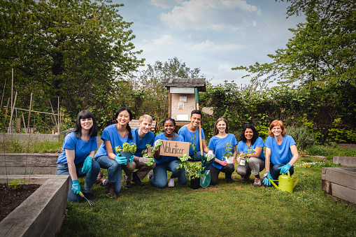 Portrait of multiracial group of diverse people kneel together smiling as volunteers for environmental project teamwork support togetherness success in community garden park in neighborhood holding sign