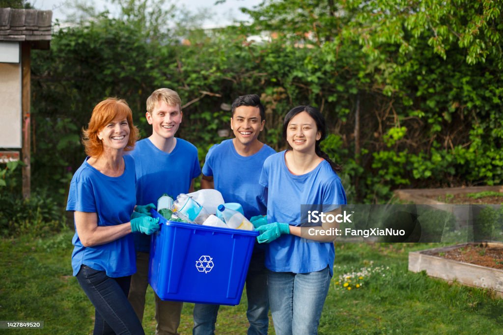 Portrait of multiracial group of young people stand with mature woman project manager leader volunteer holding recycle bin with plastic bottles within community garden park during cleanup of environment Recycling Stock Photo