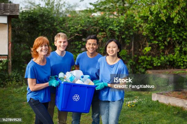 Portrait Of Multiracial Group Of Young People Stand With Mature Woman Project Manager Leader Volunteer Holding Recycle Bin With Plastic Bottles Within Community Garden Park During Cleanup Of Environment Stock Photo - Download Image Now