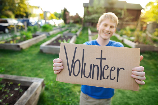 Young man stands holding volunteer sign gratitude as volunteer in community garden park in neighborhood smiling