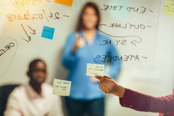 vue arrière rapprochée de la main touchant une note adhésive sur un mur de verre dans un bureau d’affaires lors d’une réunion d’idées de remue-méninges avec des collègues de travail étudiants apprenant l’éducation - adhesive note rear view business meeting photos et images de collection