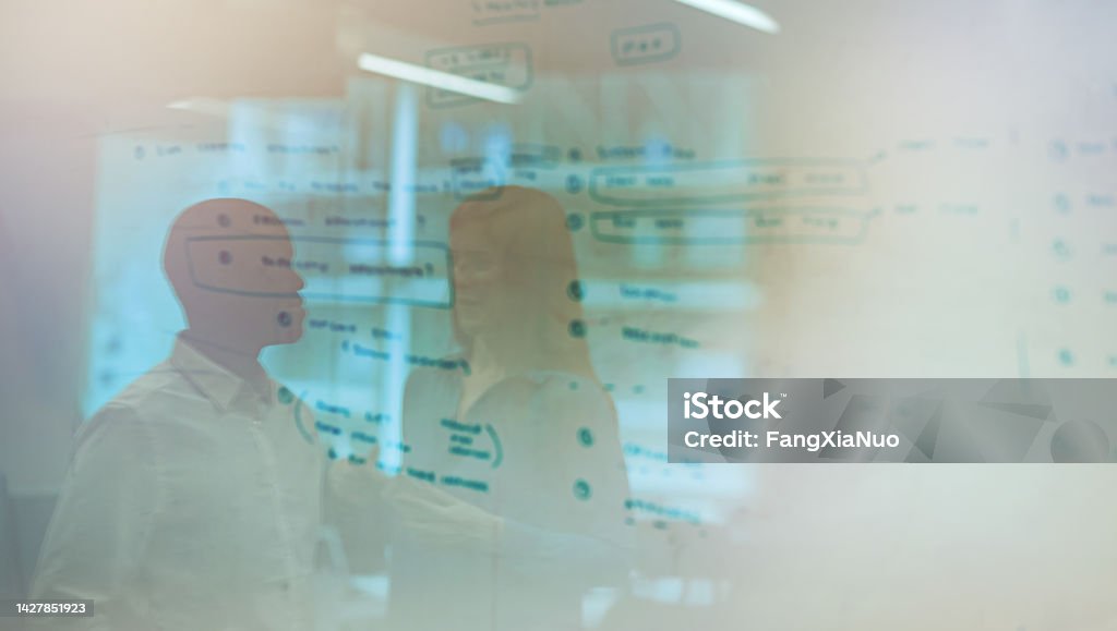 Multiracial business persons work colleagues collaborating together with whiteboard visual aid during brainstorming idea meeting in office together with reflections in glass wall Diagram Stock Photo
