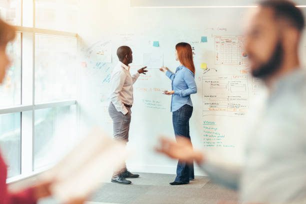 istock Multiracial group of business persons work colleagues collaborating brainstorming sharing ideas on whiteboard visual aid standing in office meeting together with reflections in glass wall 1427852061