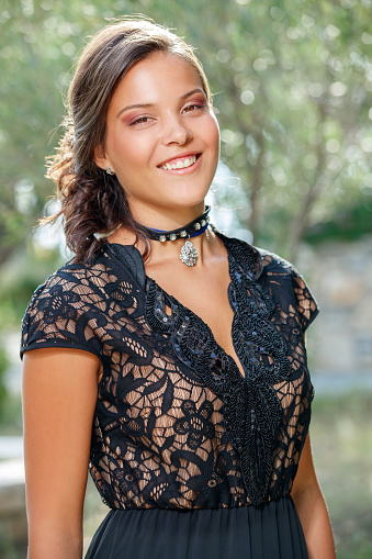 Portrait of beautiful young fashion model with long brown hair back wearing black lace top and choker, smiling at camera, beauty and fashion industry