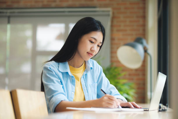 istock Young asian woman sitting at table studying and writing on notebook. 1427864053