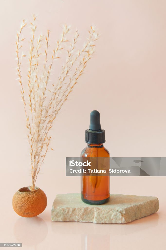Amber oil bottle with pipette on stone slab Amber oil bottle with pipette on stone slab with dry plant in dry tangerine vase. Natural cosmetics. Sustainable body care products Advertisement Stock Photo