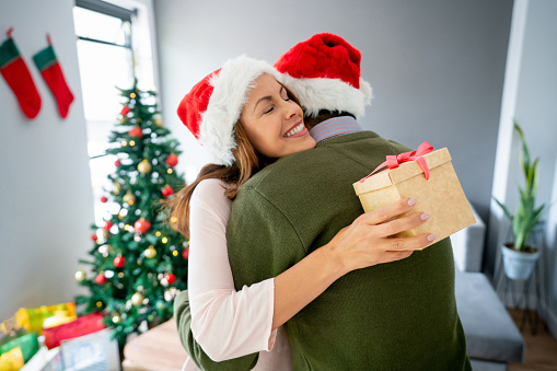 Loving Latin American couple opening presents on Christmas Day and hugging - holidays concepts