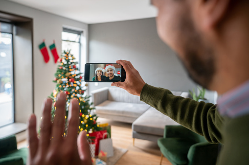 Man talking to his family on a video call on Christmas Day using his cell phone - holidays concepts