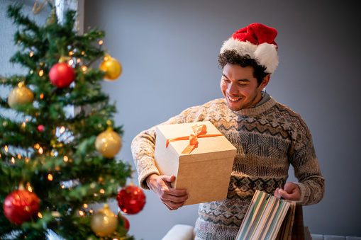 Happy man holding Christmas presents to place under the tree and smiling - holidays concepts