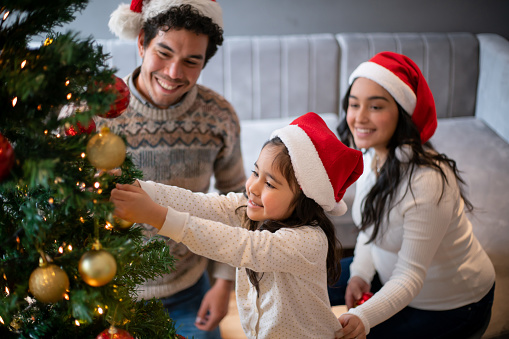 Happy Latin American family decorating the Christmas tree together at home - holidays concepts