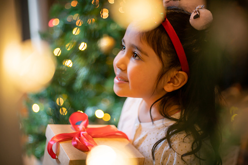 Sweet Latin American girl holding a Christmas present and smiling - holidays concepts