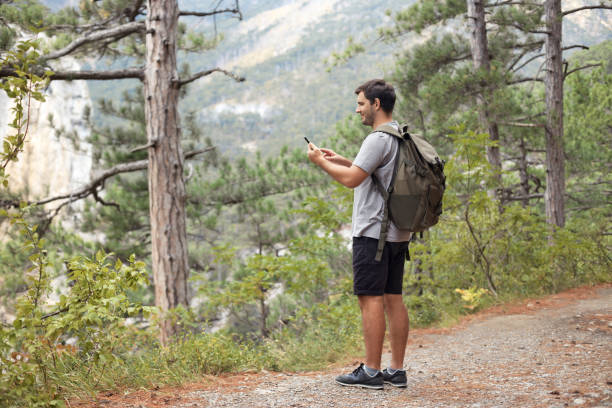 istock Full body tourist man with backpack in the mountain forest using mobile phone, looking for connection 1427883441