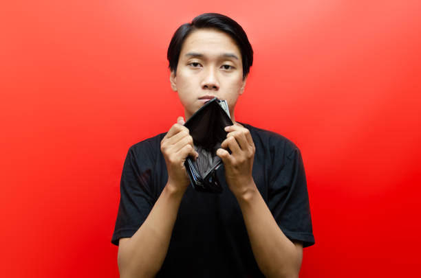Portrait of sad asian man showing  his empty wallet and looking at camera isolated over red background. bankrupt concept. jobless concept. bankrupt and jobless concept. begging currency beggar poverty stock pictures, royalty-free photos & images