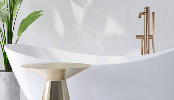 istock Gold brass side table by white ceramic bathtub in modern design bathroom and banana tree with sunlight from window and leaf shadow on white tile wall 1427889559