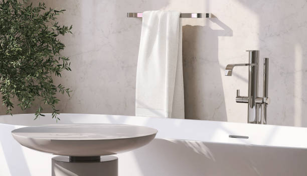 Round side table by white ceramic bathtub in modern contemporary design bathroom with sunlight from window on beige marble wall