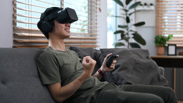 istock Joyful asian man wearing virtual reality headset, playing simulation game in living room. Future technology concept. 1427894735