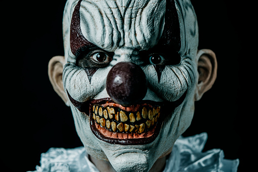 closeup of a creepy bald evil clown staring at the observer, against a black background