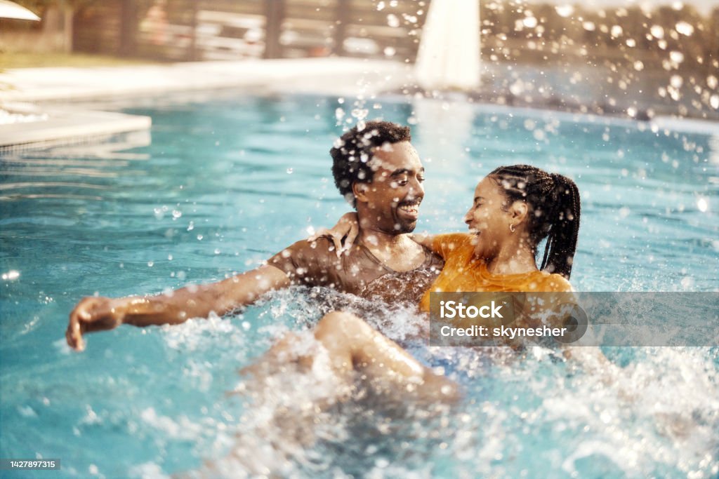 Cheerful black couple having fun in the swimming pool. Cheerful African American couple having fun during summer day in the pool. Copy space. Swimming Pool Stock Photo