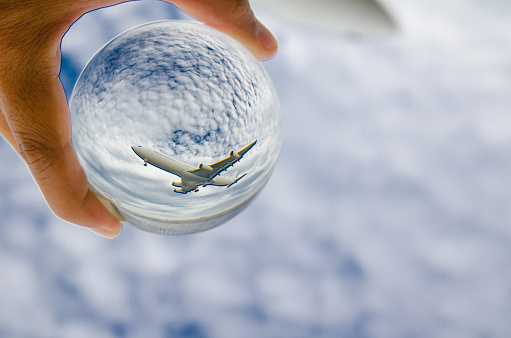 Airplane flying on cloudy sky photography in clear crystal glass ball.