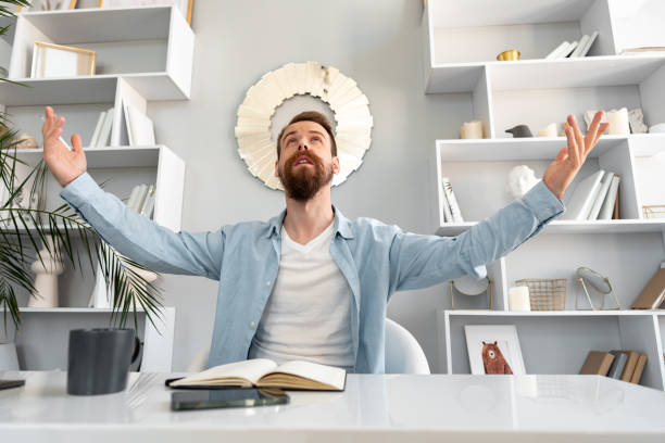 Young successful man sitting at the table raising his hands