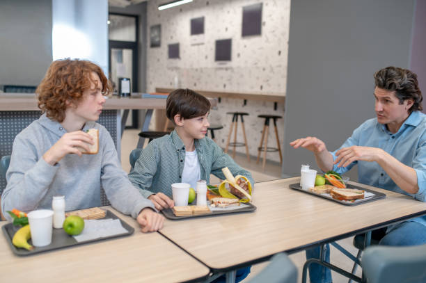Young school children eating lunch together in the cafeteria, focusing on a young boy enjoying his meal.