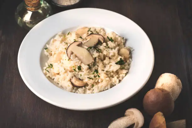 Risotto with mushrooms porcini (Boletus Edulis) on wooden dark rustic background. Healthy tradition nord Italian and French recipes, autumn and winter homemade cooking