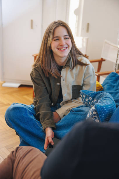 Teenage girl sitting on the sofa and talking to her friend, smiling at him stock photo