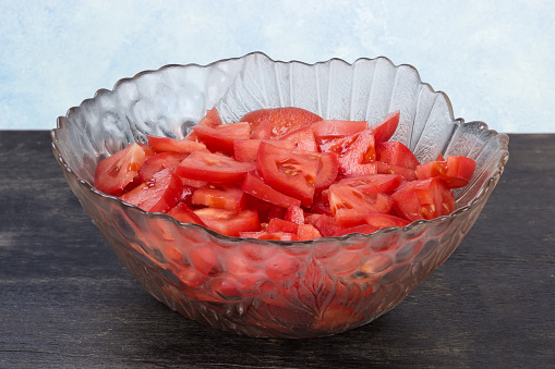 Sliced fresh red tomatoes in the glass salad bowl on a black surface