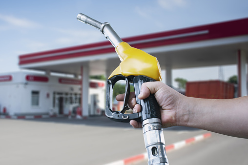 Holding a fuel nozzle against with gas station blurred background