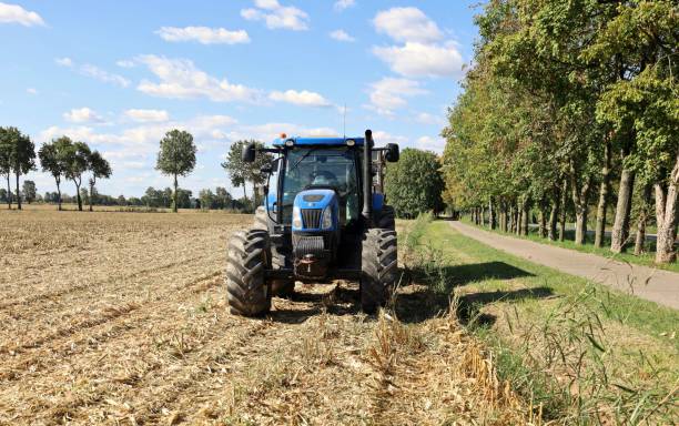 New Holland tractor on a maize field just harvested Pradamano, Italy. September 22, 2022. New Holland tractor on a maize field just harvested in early autumn. Front view. country road road corn crop farm stock pictures, royalty-free photos & images