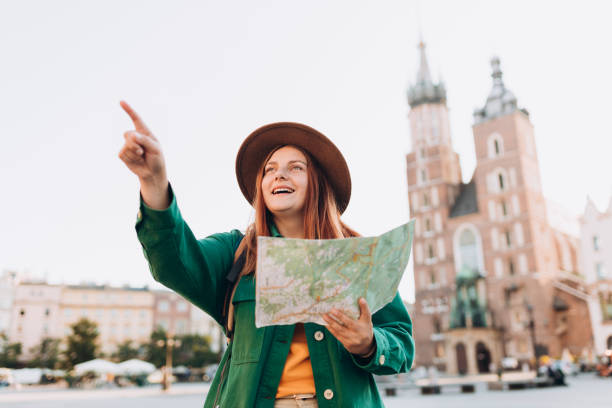 Attractive young female tourist is exploring new city. Redhead woman pointing finger and holding a map on Market Square in Krakow. Traveling Europe in autumn. St. Marys Basilica atractiva turista femenina está explorando una nueva ciudad. mujer pelirroja señalando con el dedo y sosteniendo un mapa de papel en la plaza del mercado de cracovia. viajando por europa en otoño. basílica de santa maría. estilo de vida activo