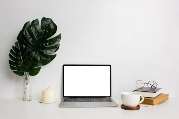 istock Working space with computer, green leaves, coffee cup and book over the white table. 1427927301