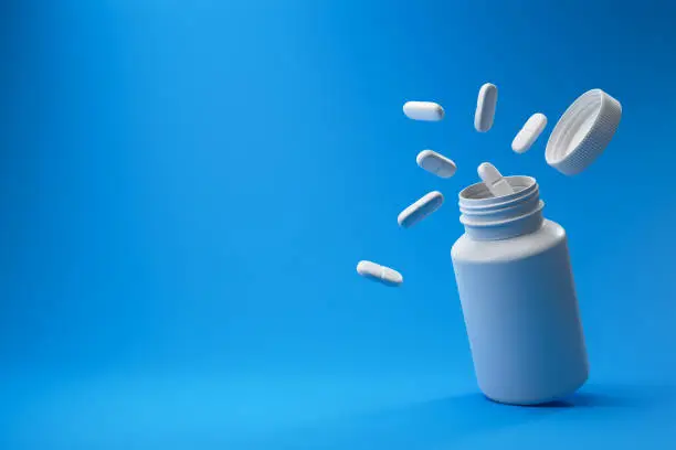Photo of White pills and plastic medical container on a blue background.