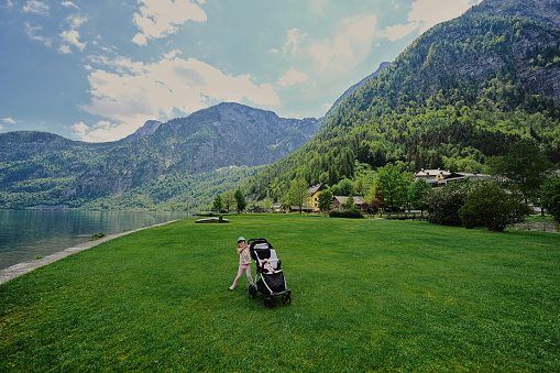 Baby girl with stroller against beautiful scenic landscape over Austrian alps lake in Hallstatt, Salzkammergut, Austria.