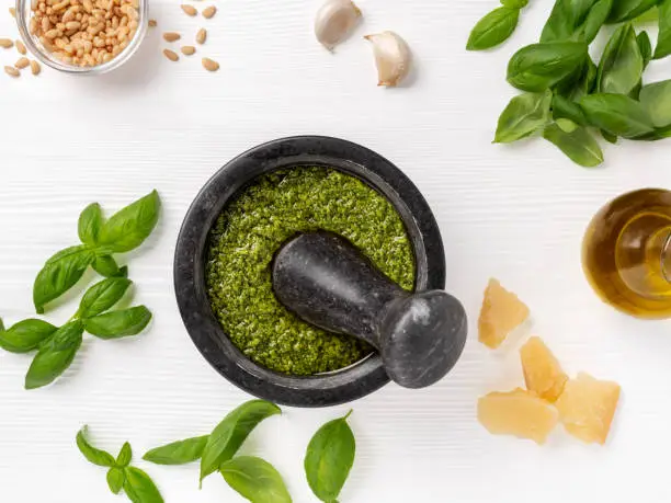 Pesto sauce ingredients such as fresh basil, olive oil, parmesan cheese, pine nuts and garlic. Mortar and pestle is used to crush and mix ingredients.